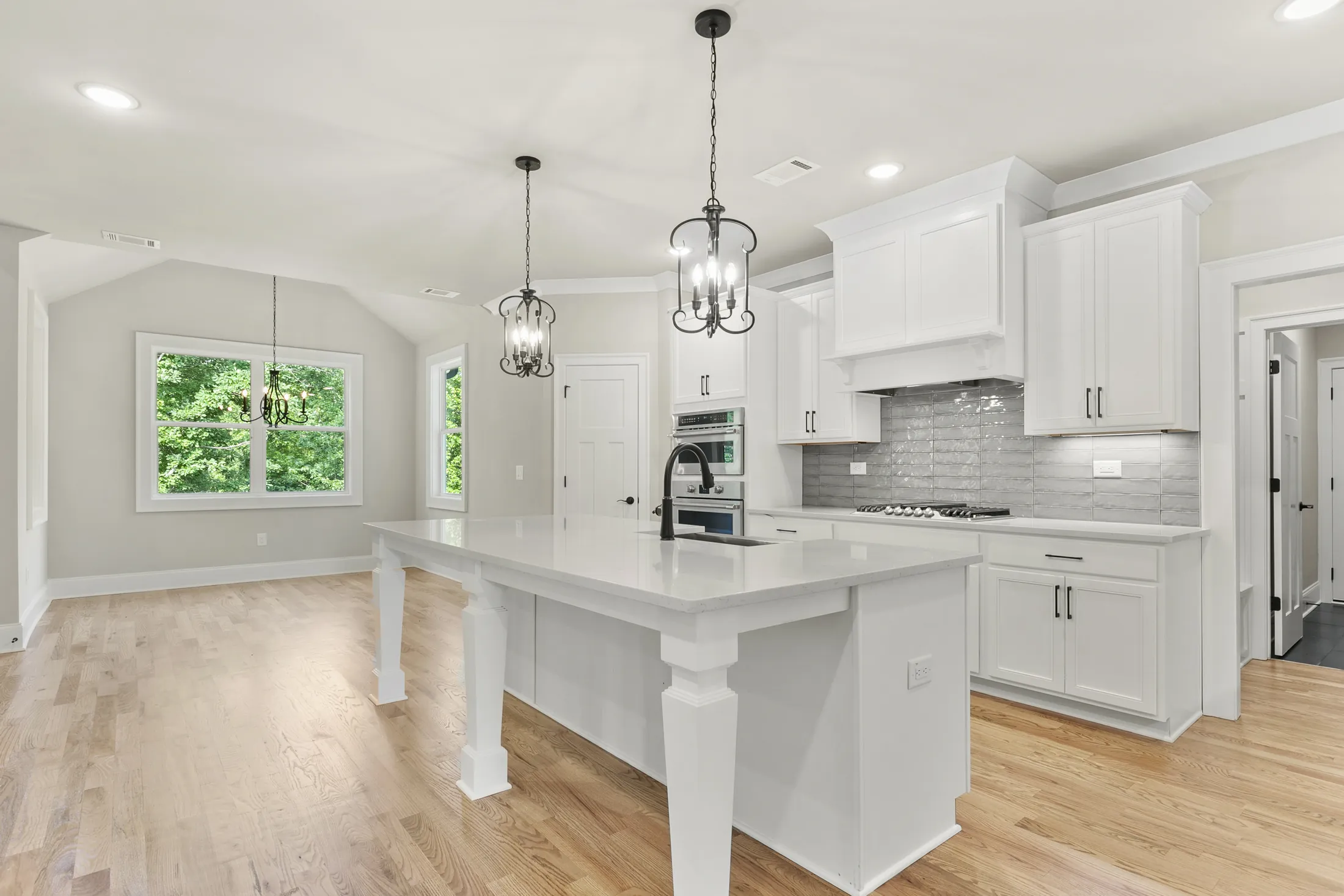 White kitchen with a large island, pendant lights and hardwood floors