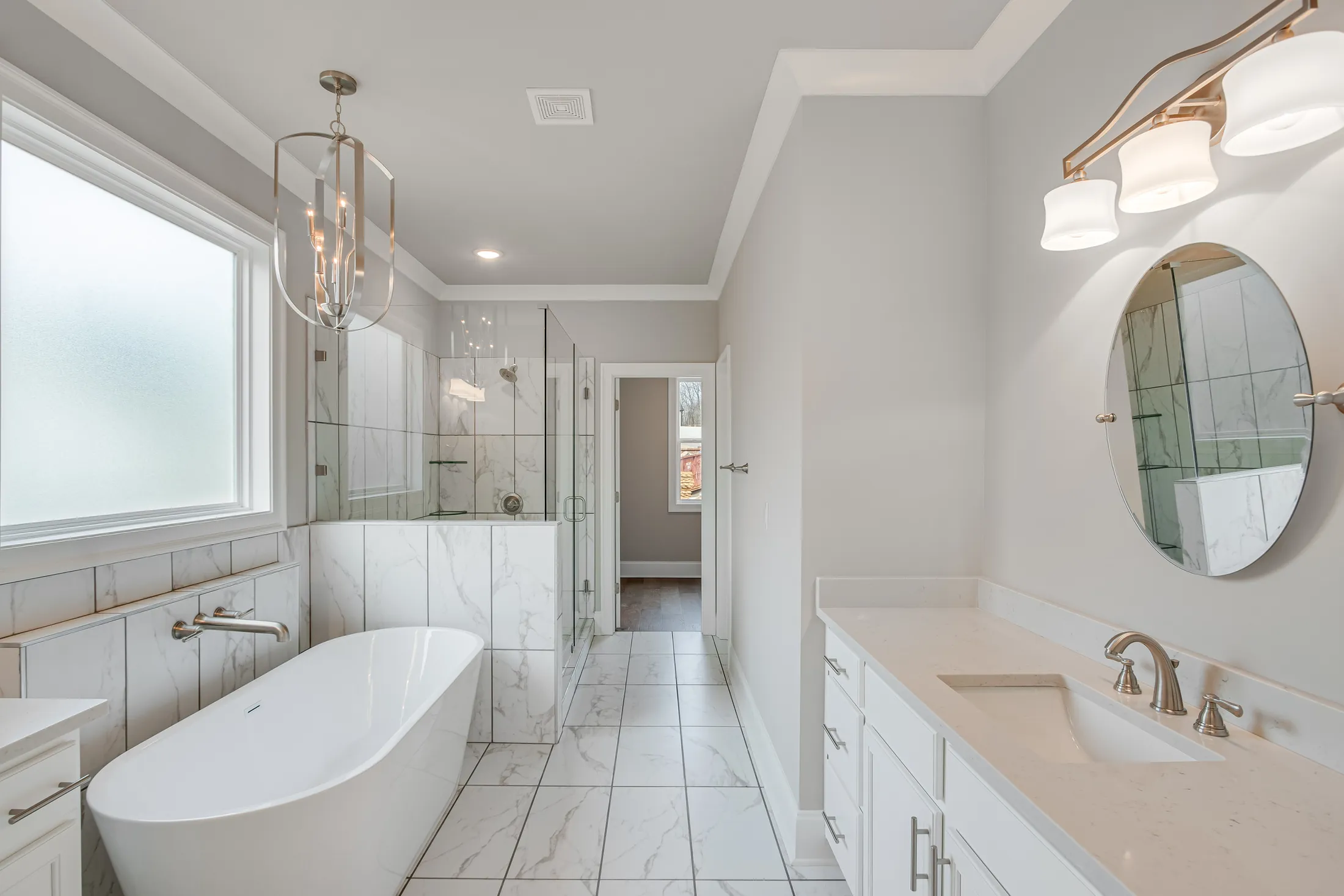 Primary bathroom with a freestanding tub, a pendant light and marble-look tile