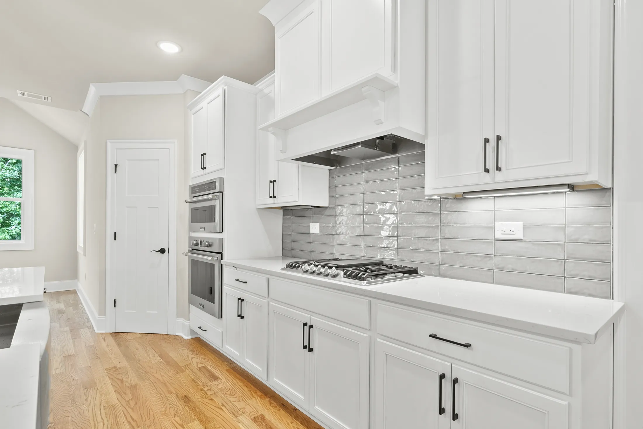 Kitchen with white cabinets, a wall oven and a gray tile backsplash