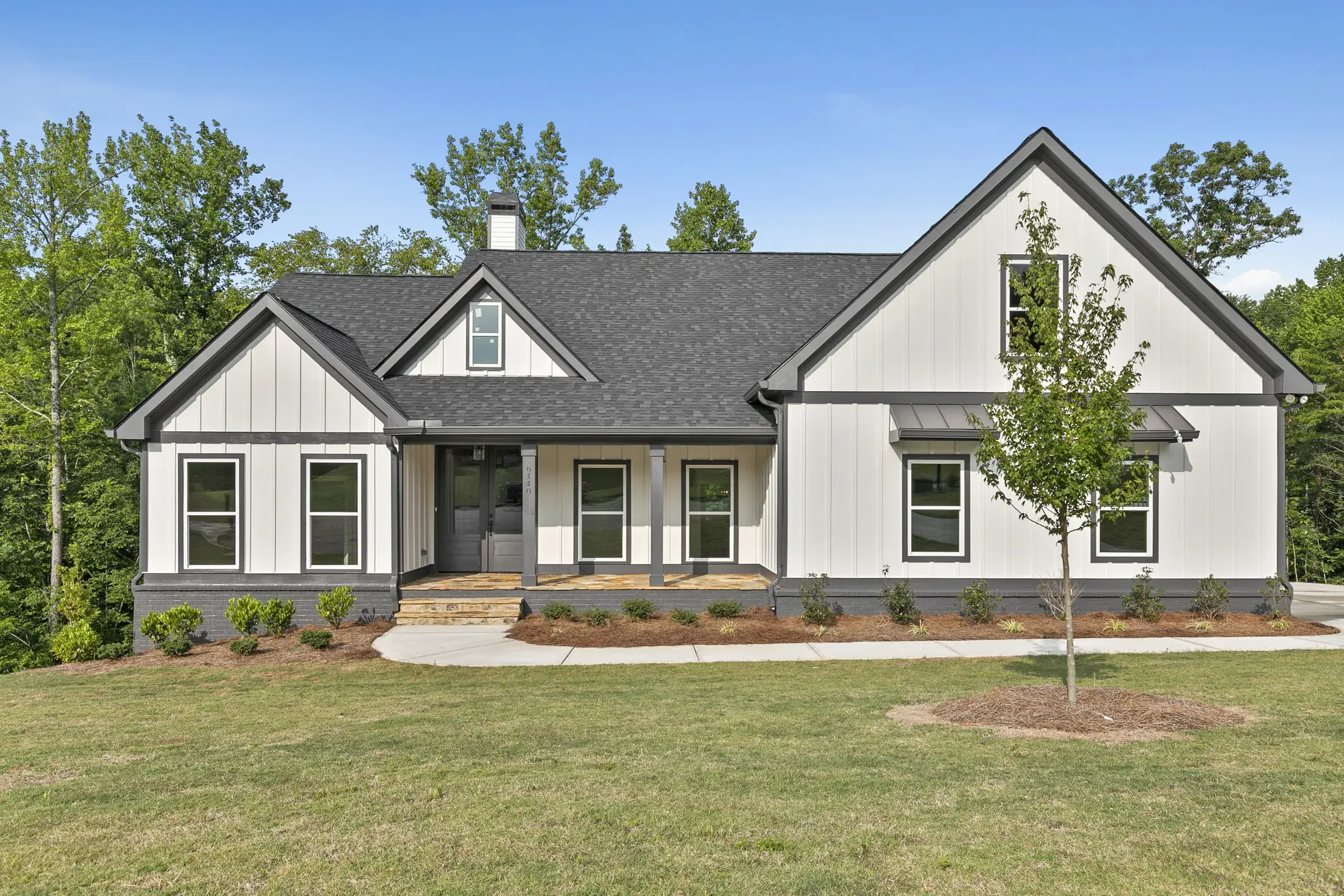 Single-story custom home with a covered porch, board-and-batten siding and a young tree
