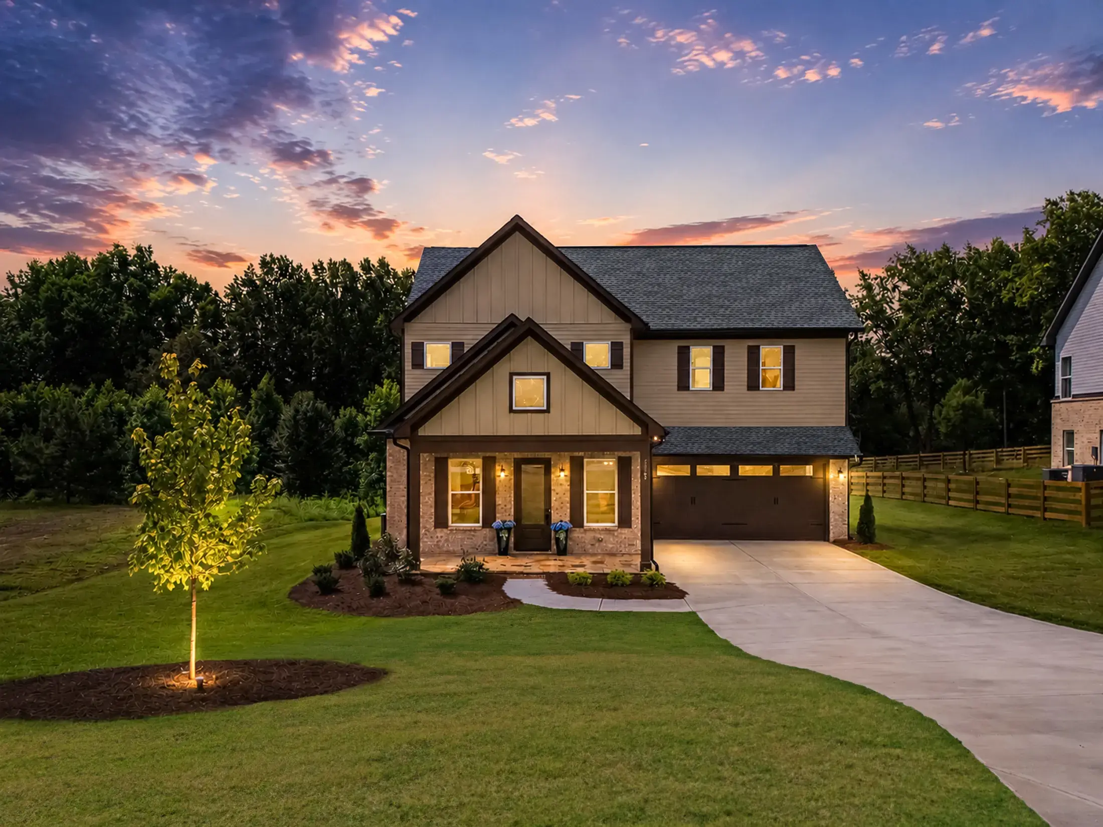 Custom home with a covered front porch and attached garage glowing at dusk