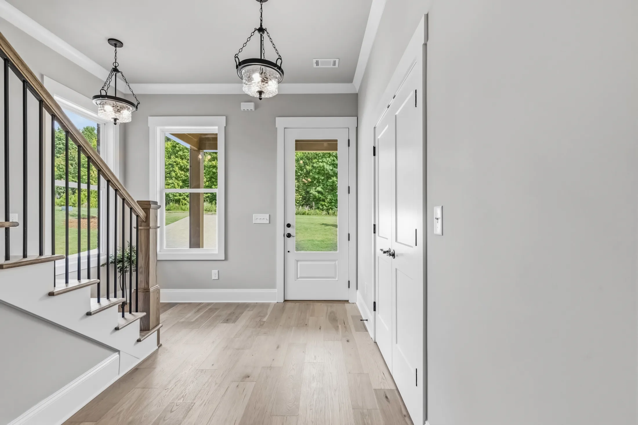 Entry foyer with two pendant lights, a staircase and a glass-paneled front door
